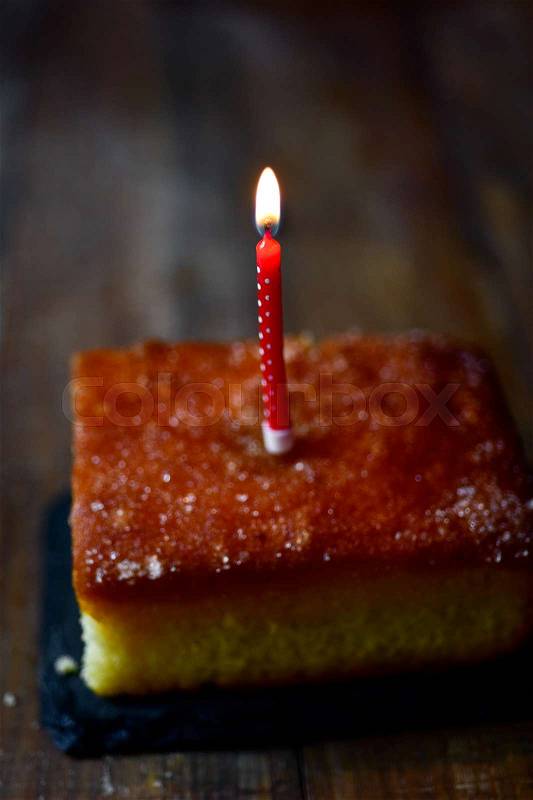 Closeup of a cake topped with a lit birthday candle on a rustic wooden table, stock photo