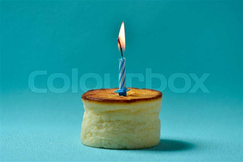 A cheesecake topped with a lit birthday candle on a blue background, stock photo