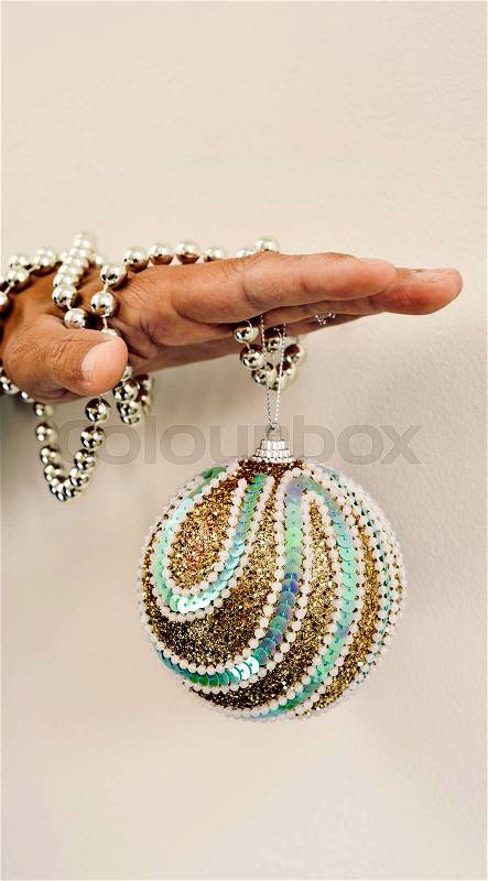 An elegant christmas ball hanging from the hand of a young caucasian man ornamented with a silvery beaded garland, stock photo