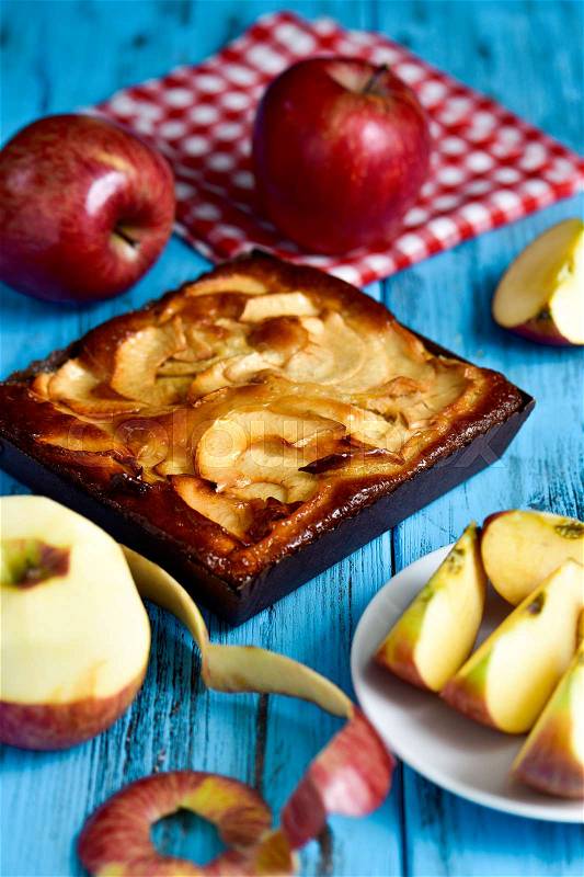 Closeup of an apple cake and some red apples on a blue rustic wooden table, stock photo