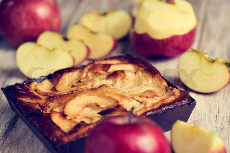 Closeup of an apple cake and some red apples on a rustic wooden table, stock photo