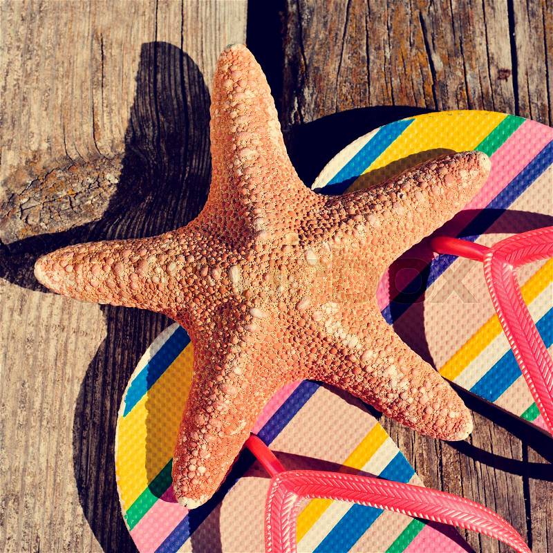 Closeup of a pair of colorful flip-flops and a starfish on a weathered wooden pier, stock photo