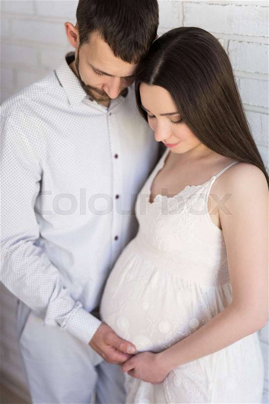 Family, pregnancy and parenthood concept - close up portrait of happy pregnant couple posing over white brick wall, stock photo