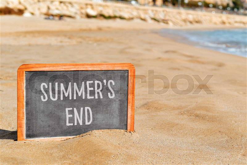 Closeup of a chalkboard with the text summers end written in it, on the sand of a beach, stock photo