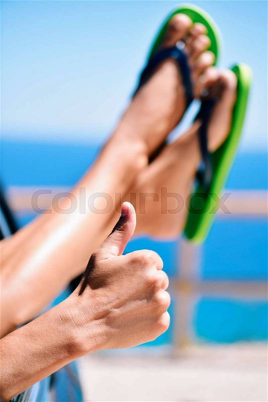Closeup of of a young caucasian man wearing flip-flops relaxing in a car near the ocean, giving a thumbs up sign, stock photo