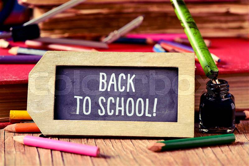Label-shaped chalkboard with the text back to school, some old books and old stationery such as a pen nib or some pencil crayons of different colors, on a rustic wooden table, stock photo