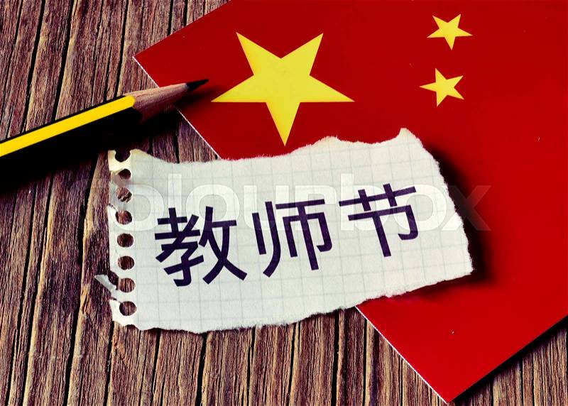 Closeup of a peace of paper with the text Teachers Day written in Chinese, a pencil and the flag of China, placed on a rustic wooden surface, stock photo