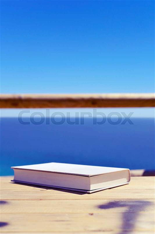 Closeup of a book with a gray cover on a wooden table outdoors, with the ocean in the background, stock photo