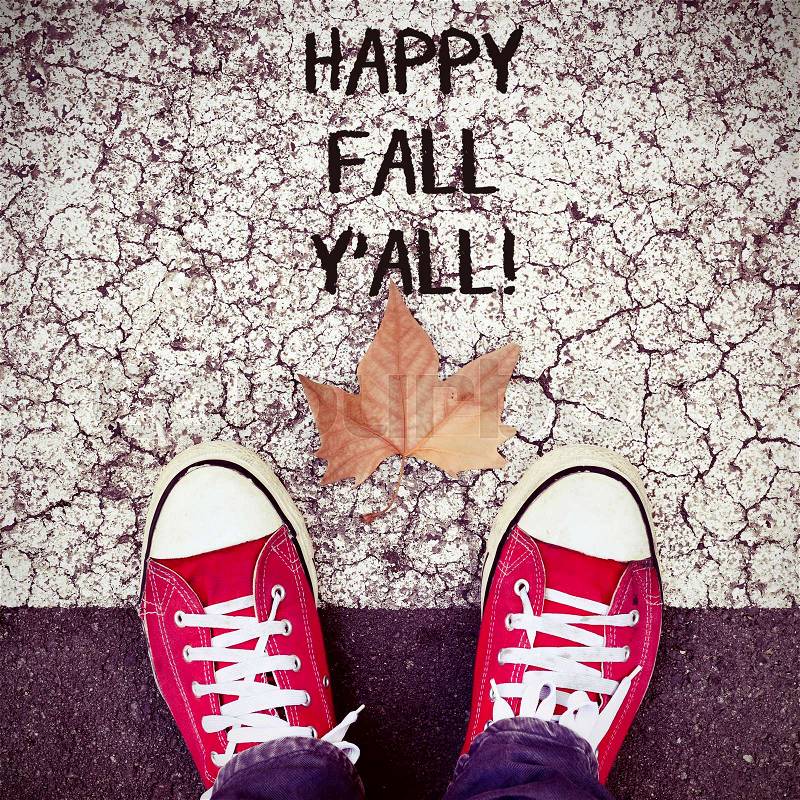 High-angle shot of a dry leaf and the feet of a man wearing red sneakers on the asphalt, and the text happy fall yall, stock photo