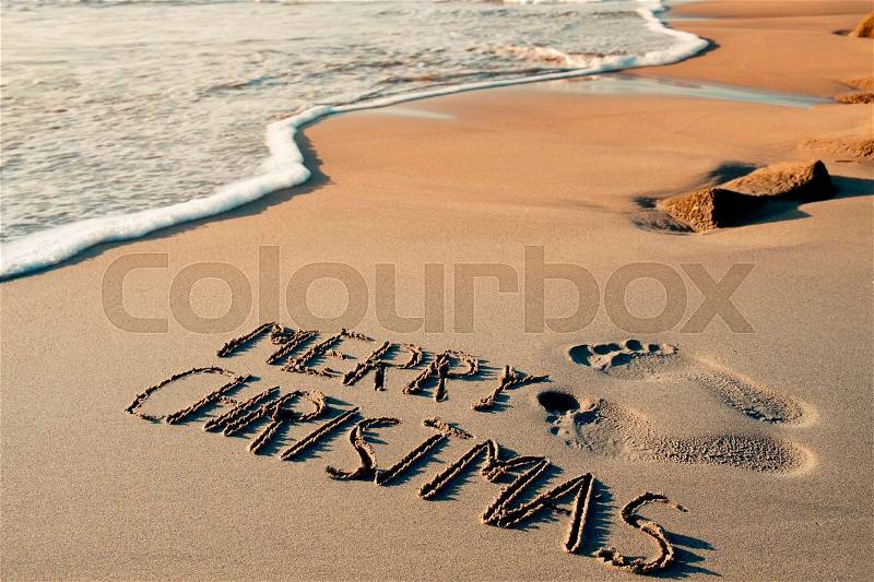 Some foot prints and the text merry christmas written in the sand of a beach, stock photo