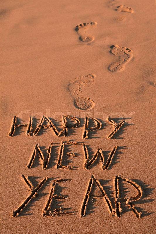 Some foot prints and the text happy new year written in the sand of a beach, stock photo