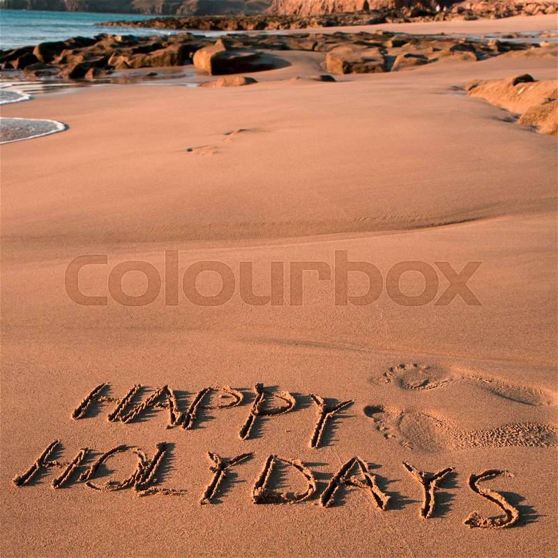Some foot prints and the text happy holidays written in the sand of a beach, stock photo