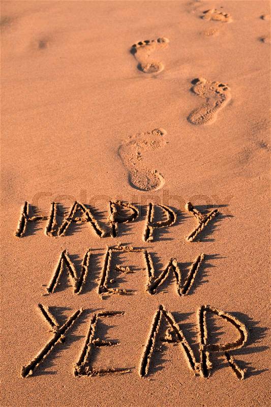 Some foot prints and the text happy new year written in the sand of a beach, stock photo