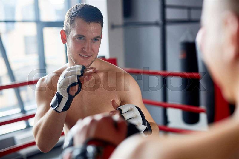 Portrait of smiling shirtless man practicing boxing with sparring partner in fighting club, stock photo