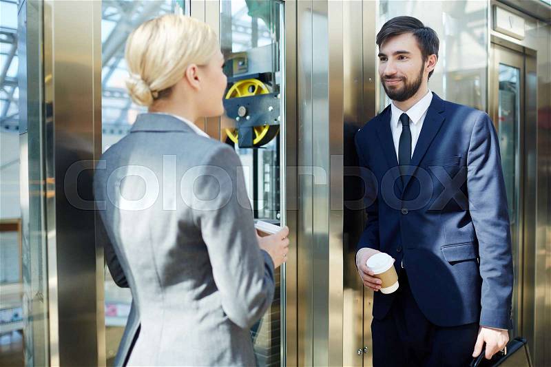 Portrait of two business colleagues, man and woman, chatting in elevator of modern office building, stock photo