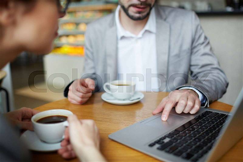 Portrait of two business people meeting in cafe and using laptop at table, finger on touchpad closeup, stock photo
