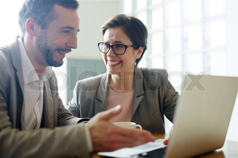 Portrait of two business people, man and woman, laughing while looking at laptop screen during meeting in cafe, stock photo