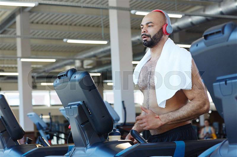Sporty man jogging on treadmill in gym, stock photo