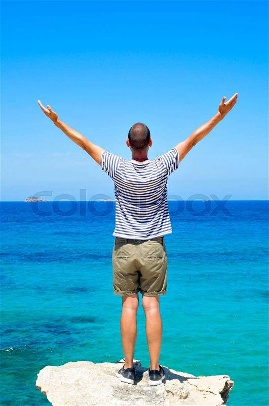 A young man, seen from behind, with his arms in the air in front of the ocean, feeling free, stock photo