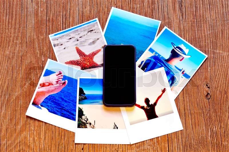 High-angle shot of a smartphone and some photos, shot by myself, of a young man in the beach and some other beach scenes, placed on a rustic wooden table, stock photo