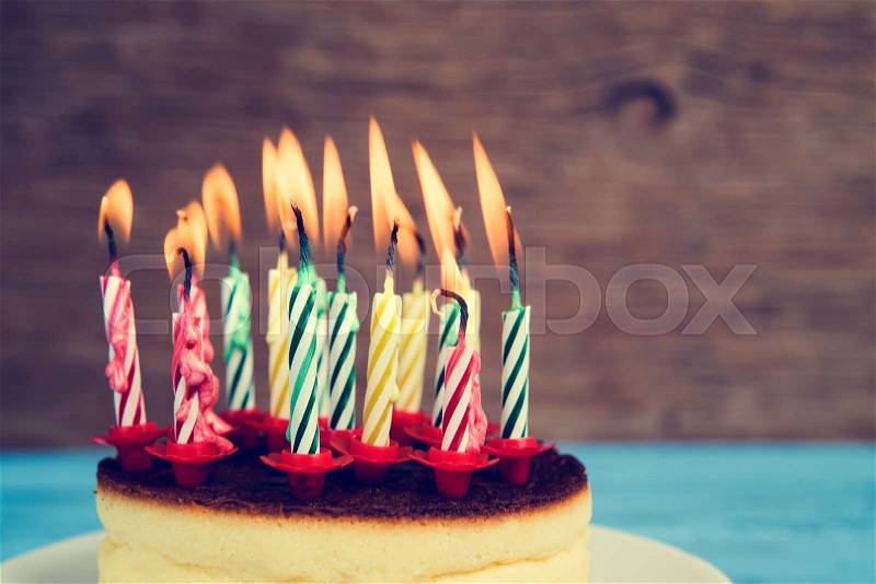 Closeup of a cheesecake with some lighted birthday candles of different colors, with a retro effect, stock photo