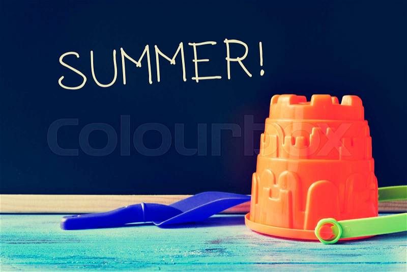 A blue toy shovel and an orange toy pail on a blue school desk, and the word summer written in a chalkboard, stock photo