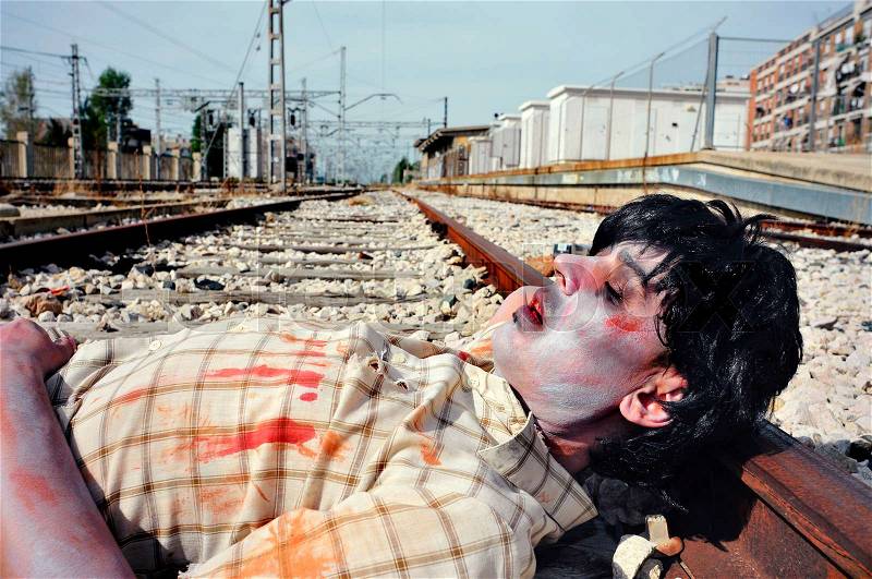 Closeup of a scary zombie man lying down at the railroad tracks, stock photo