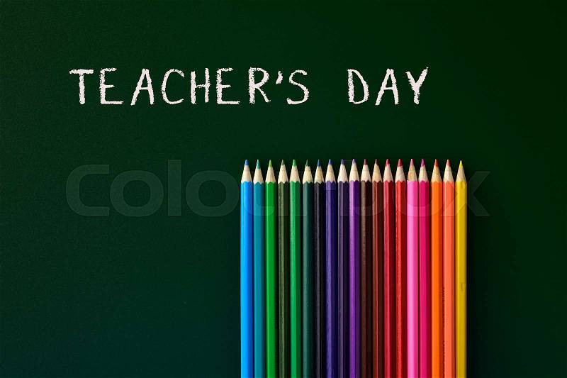 Some coloured pencils of different colors and the text teachers day written in a green chalkboard, stock photo
