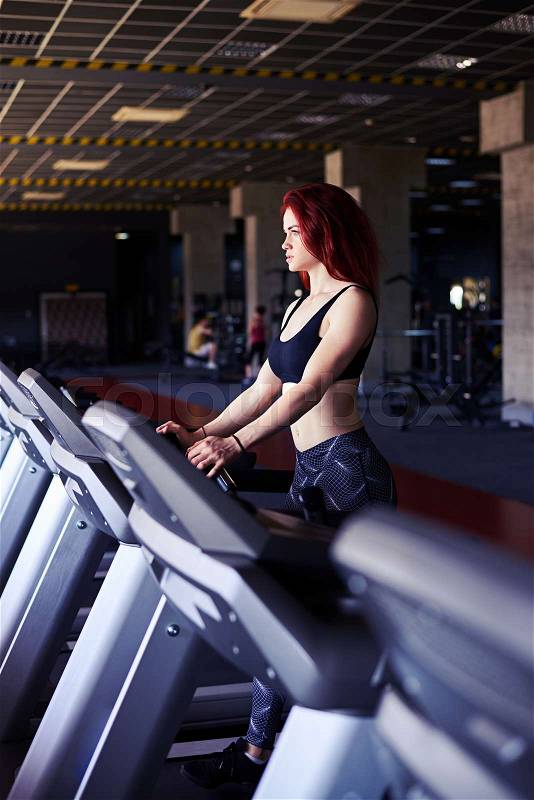 Side view of determined slim girl running on treadmill at the gym, engaged in fitness sport club, stock photo