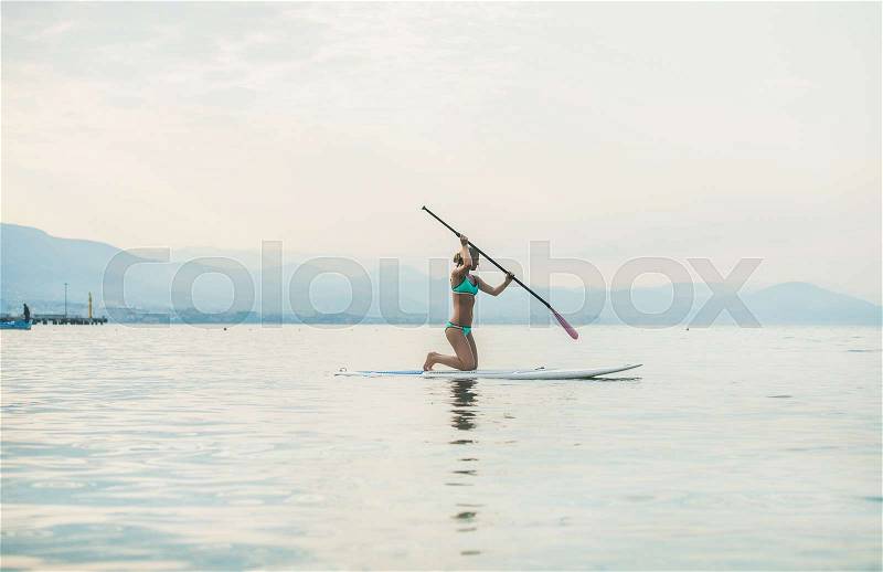 Young beautiful slavian woman tourist practicing paddle boarding in sea at beach near ancient fortress wall and shipyard in city center of Alanya, Mediterranean Turkey, stock photo