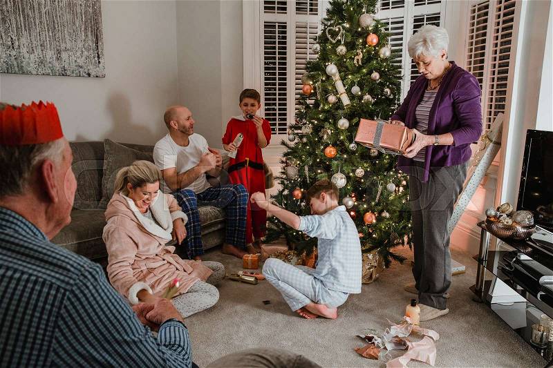 Three generation family are opening presents together on christmas morning. They are sitting by the christmas tree in the living room of their home, wearing pyjamas. , stock photo