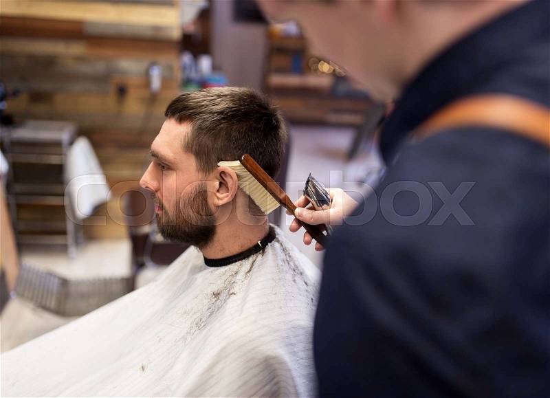 Grooming, hairdressing and people concept - man and barber with trimmer and brush cleaning hair at barbershop, stock photo