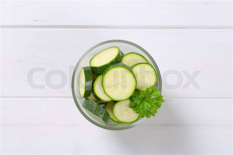 Glass of green zucchini slices on white wooden background, stock photo