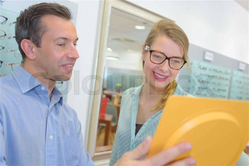 Experienced male optician offering glasses frames to pretty client, stock photo
