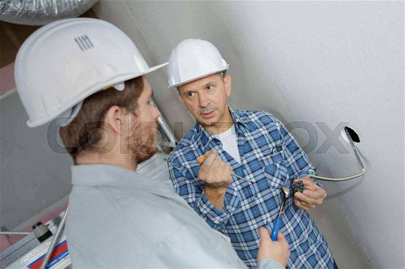 Friendly master electrician and apprentice working, stock photo