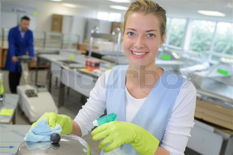 Female cleaning industrial kitchen coleague in the background, stock photo