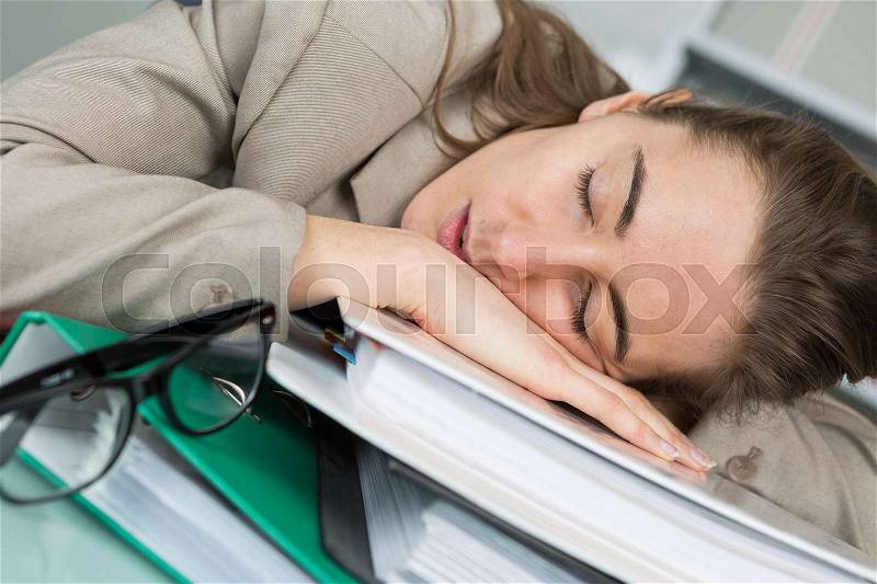 Female employee sleeping on her desk at the office, stock photo