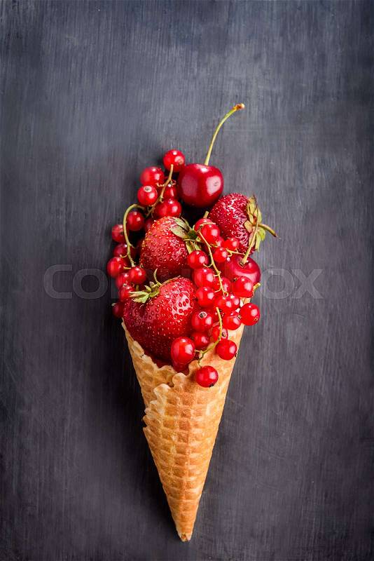 Fresh red summer berries - strawberries, red currants, cherries in the waffle cone in the form of ice cream on the black wooden background. Healthy dessert concept. Top view. Space for text, stock photo
