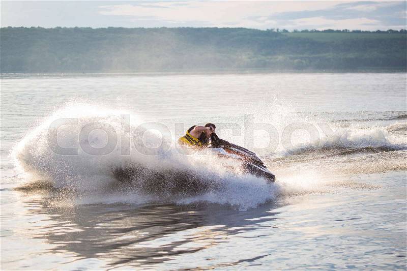 A man driving a jet ski , stunting and making spray of water drops with a sunlight on background, stock photo