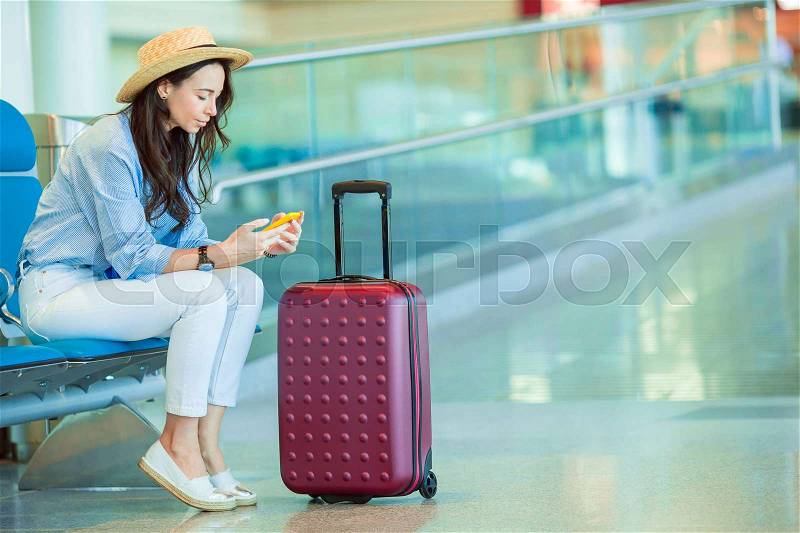 Airline passenger in an airport lounge waiting for flight aircraft. Caucasian woman with smartphone in the waiting room, stock photo