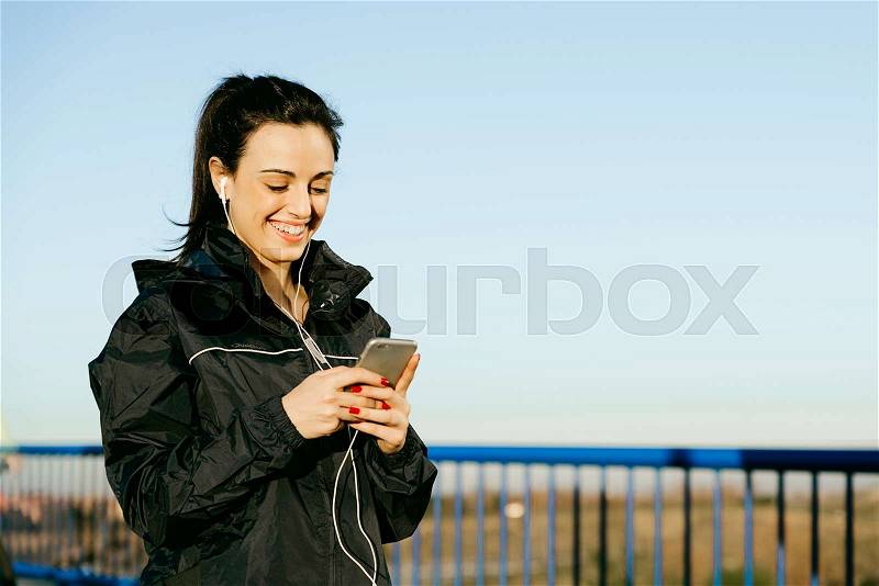 Young woman runner is having break and listening to music during the run in city, stock photo