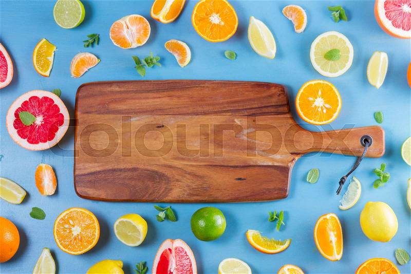 Citrus food frame pattern on blue background - assorted citrus fruits with mint leaves, copy space on wooden cutting board, stock photo