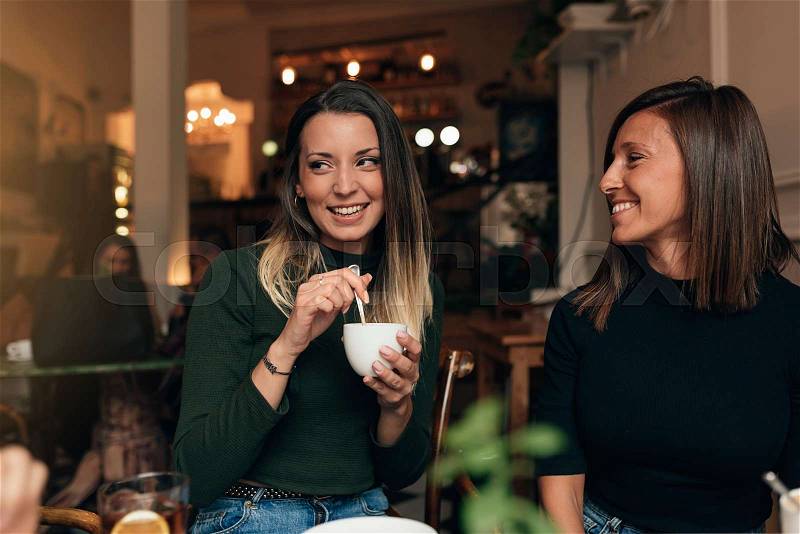 Two beautiful women drinking coffee and chatting in cafe, stock photo