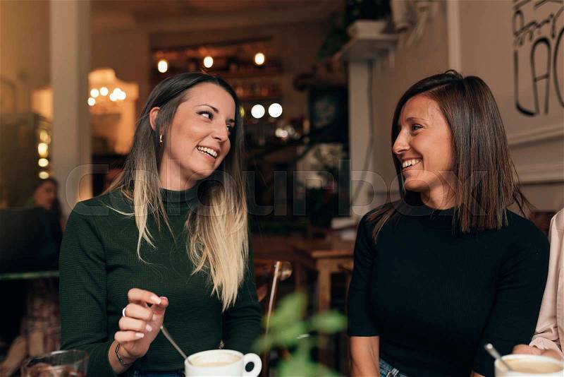 Two beautiful women drinking coffee and chatting in cafe, stock photo