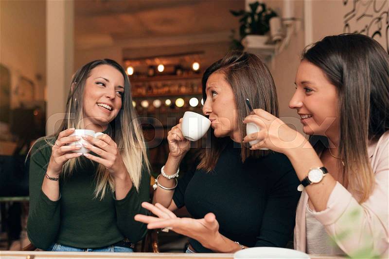 Three beautiful women drinking coffee and chatting in cafe, stock photo