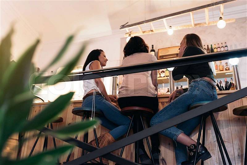 Three beautiful women drinking coffee and chatting in cafe, stock photo