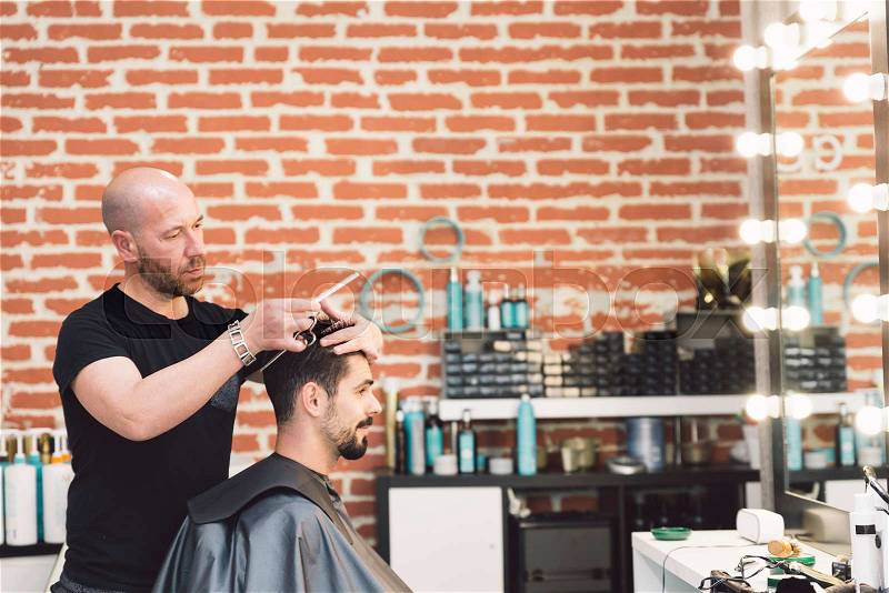 Hairstylist making men\'s haircut to an attractive man in the beauty salon, stock photo