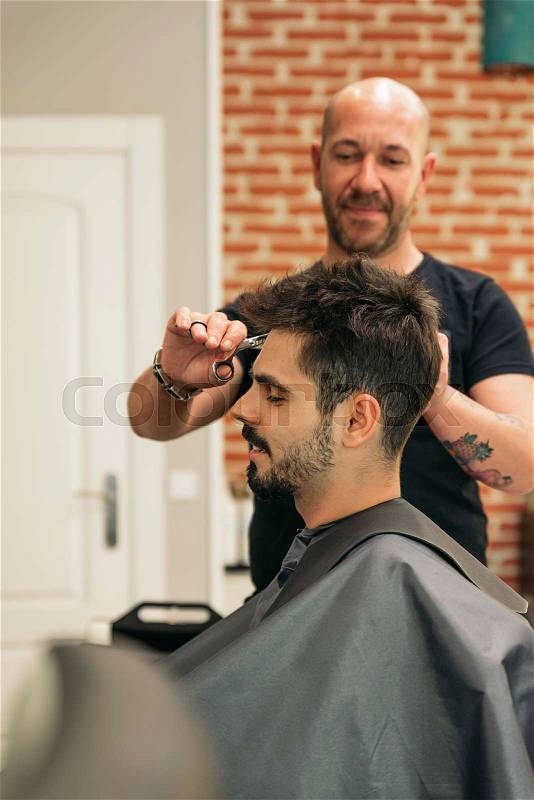 Hairstylist making men's haircut to an attractive man in the beauty salon, stock photo