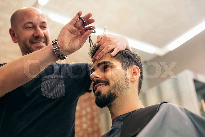 Hairstylist making men's haircut to an attractive man in the beauty salon, stock photo