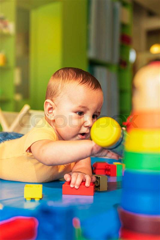 Happy baby playing with toy blocks in the kindergarten, stock photo